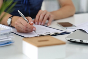 Close up of a woman in an office writing on a clipboard