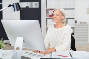 Senior businesswoman at work in the office seated at her desk typing in information on the desktop computer