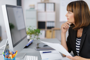 Side View of a Businesswoman Looking at her Computer Screen Seriously While Holding Documents.