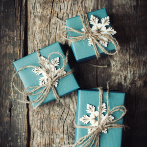 Three Festive Boxes in Blue Paper Decorated with Snowflakes and Linen Cord on Wooden Table. 