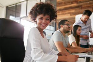 Portrait of attractive young woman sitting at conference room with colleagues in background.