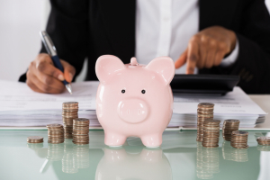 Closeup of business woman calculating her savings with a piggy bank and stacks of coins