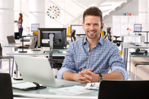 Happy successful business consultant at startup office, sitting at the table with laptop.