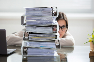 Close-up Of A Businesswoman Hiding Behind The Stack Of Folders On Desk At Workplace
