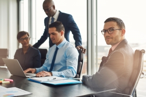 Professional young multiracial business team seated working around a table in the office with a young man in the foreground turning to look at the camera